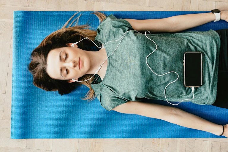 A woman lying on a yoga mat with headphones in and her eyes closed.