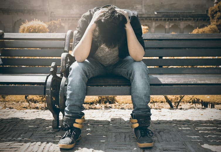A man sits on a bench with his head in his hands.