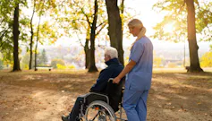 nurse walks with an elderly man in a wheelchair