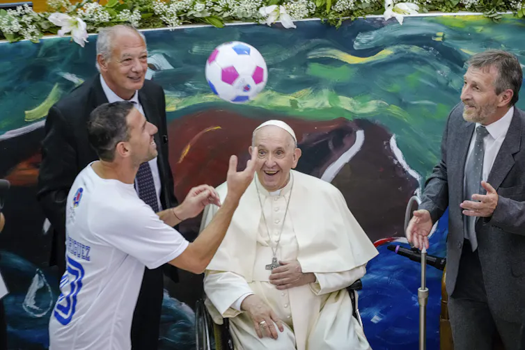 The pope smiles at the soccer player.