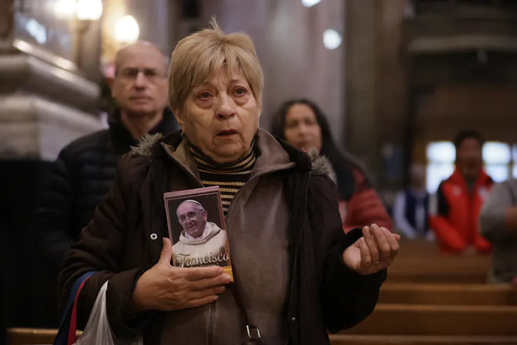 A woman holds a photo of Francis and prays.