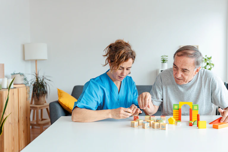 A medical person with an elderly patient in a care home, doing a puzzle together.