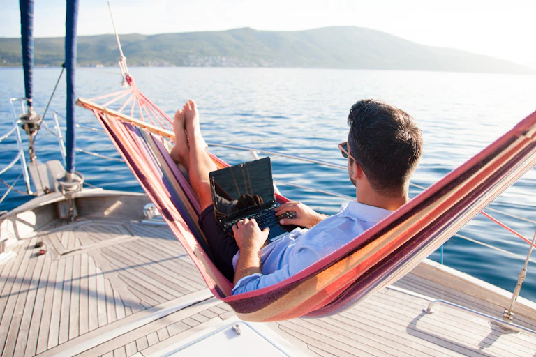 Man in hammock on yacht working on laptop