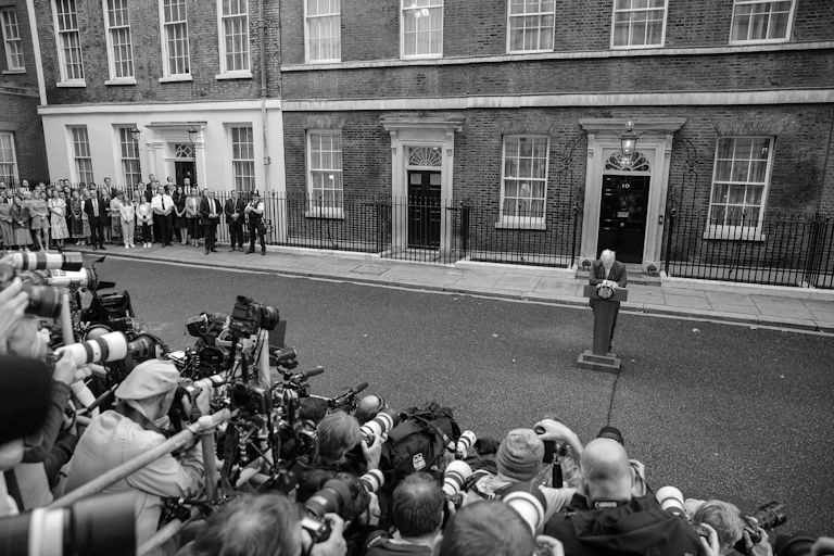 Wide angle, black and white photo of a crowd of journalists facing Boris Johnson, speaking at a podium in front of Number 10