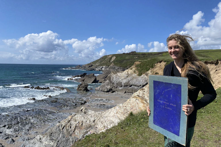 Woman Ruth Thustan standing on coastal cliff holding big blue book
