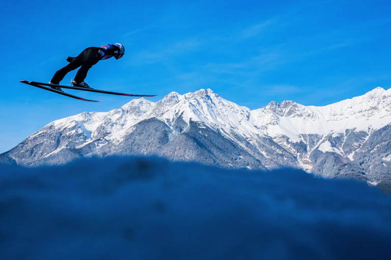 A ski jumper descending a mountain against a blue sky.