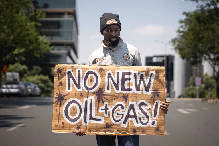 A man stands in the street with a sign reading "No new oil and gas"