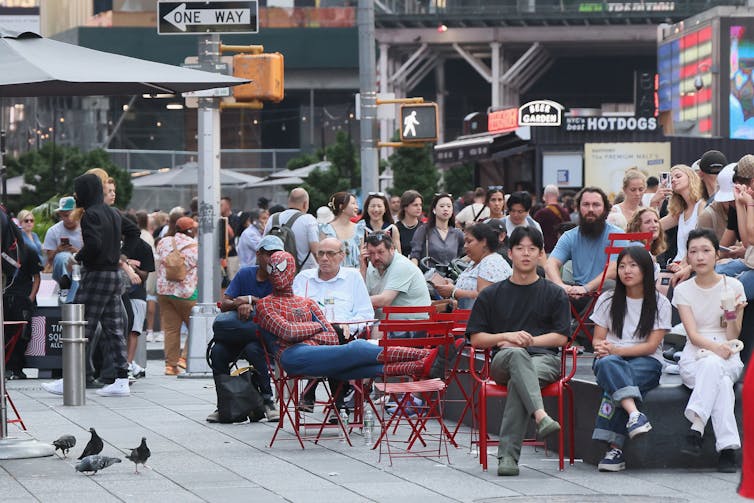 A man dressed in a Spider-Man costume sits among a crowd of onlookers.