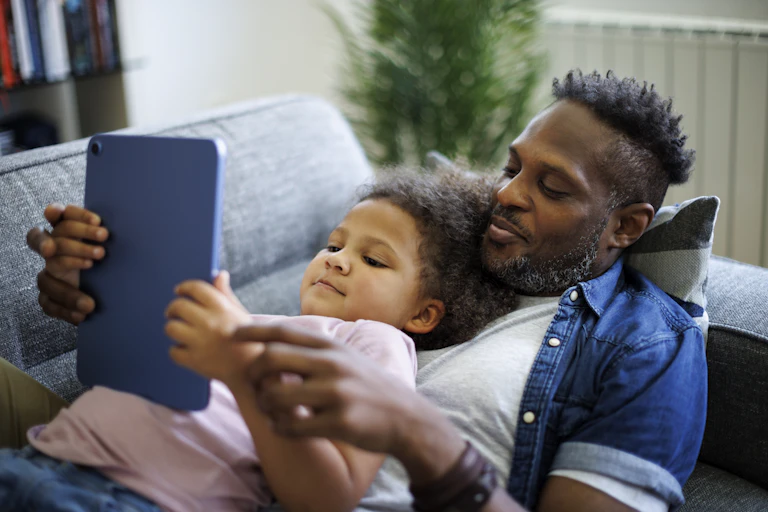 Father and child watch a tablet together on the sofa