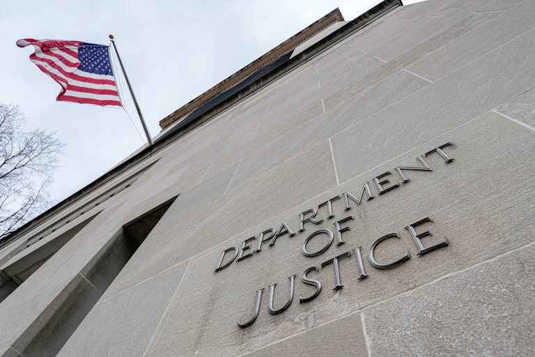 A flag flies next to a grey building that says Department of Justice.
