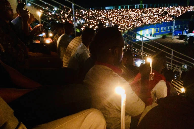 People seated in a darkened stadium holding up lit candles