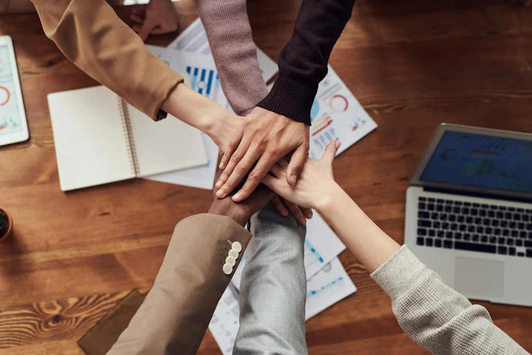 Overhead view of people's hands piled on top of one another over a desk