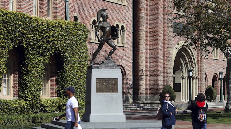 People walk past a Trojan statue.