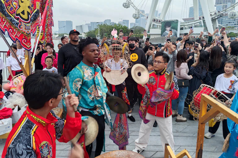 A man in traditional Chinese garv stand next to a man with cymbals.