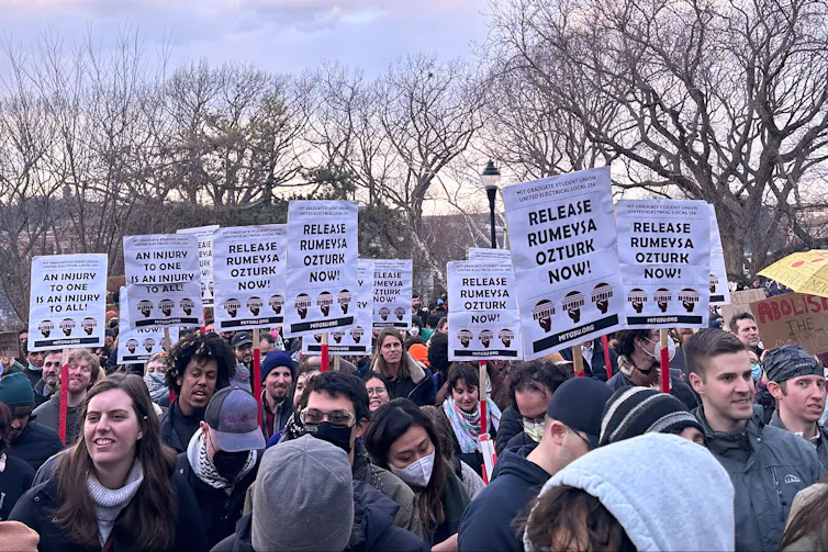 A crowd of protesters outside holding signs.