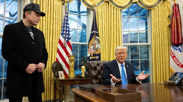 Two men, one standing and the other seated, in an ornate office