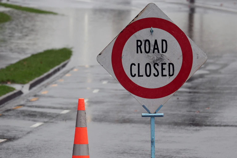 A traffic cone and a "road closed" sign on a flooded road