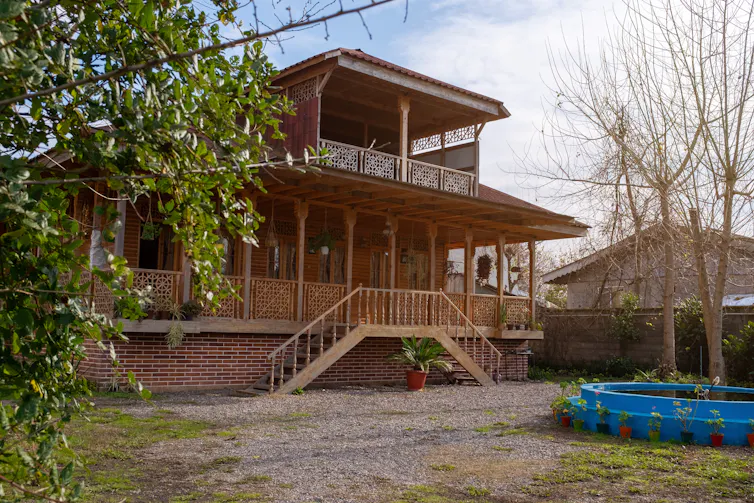 House with brick foundation, intricate wooden railings, and a sloped roof.