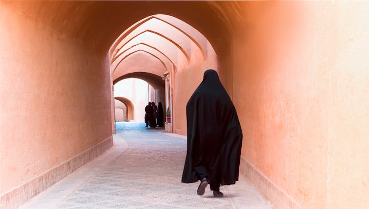 A Muslim woman walking on the narrow street of old adobe Yazd city.