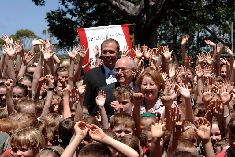 A crowd of waving school children surround the three adults.