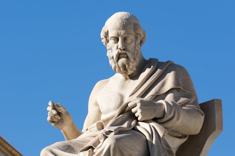 White seated statue of the philosopher Plato set against a blue sky