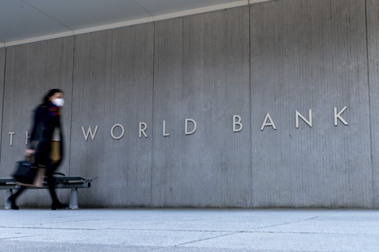 A woman in a mask walks past a grey building