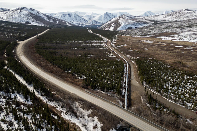 A large metal pipe stretches from mountains in the distance under a road in the foreground.