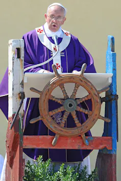 Pope Francis I delivers a speech while standing at a lectern shaped as a ship's helm.
