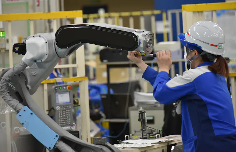 A woman in a hard hat works with a robotic arm.