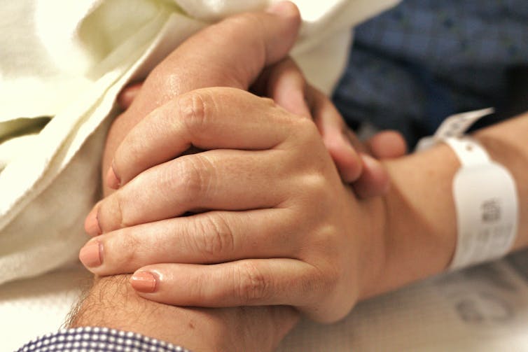 Hand with hospital band around wrist holding another hand