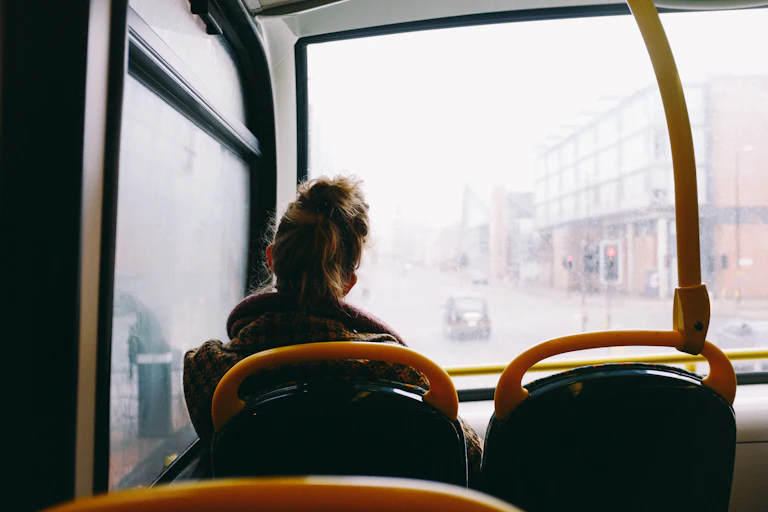 View from behind of a woman sitting in the front top row of a bus on a grey day