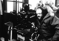 A man behind a movie camera with people behind him.
