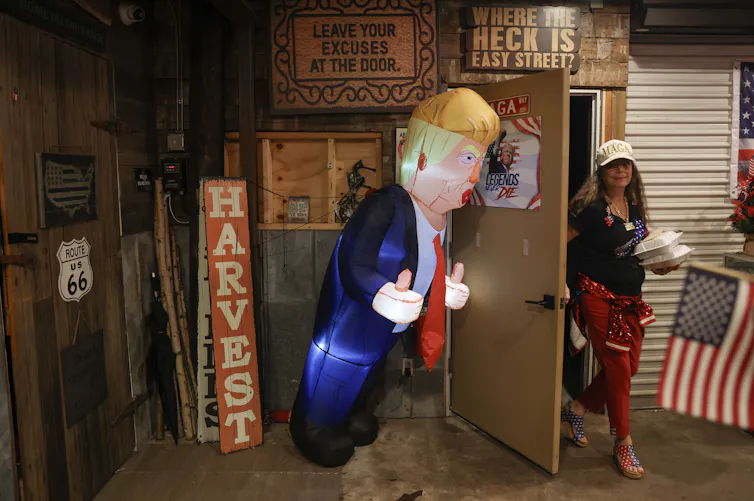 A woman walks out of a door that has a large blow-up balloon of Donald Trump.