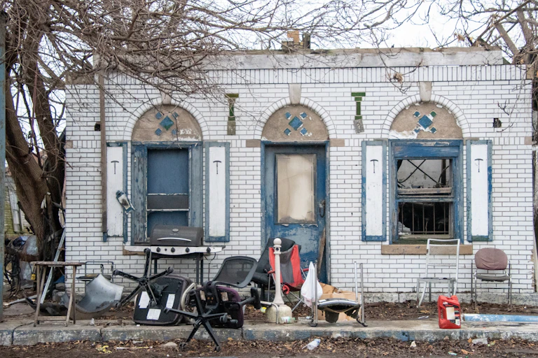 A run-down white brick building is surrounded by trash.