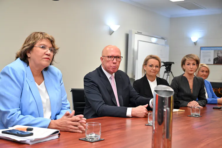 A man and three women sit at a large boardroom table.