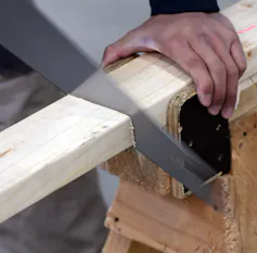 An apprentice carpenter saws wood