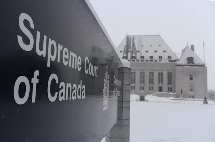 A sign reading Supreme Court of Canada in the foreground with the court building in the background in winter
