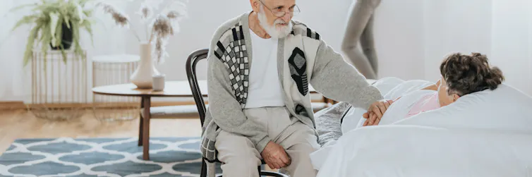 A man with gray hair sits by a woman's bedside