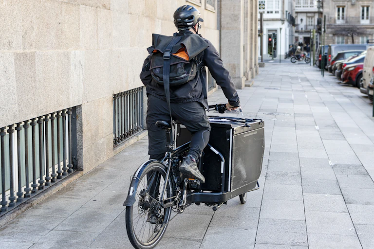 Coursier de dos à vélo-cargo dans une rue en ville.