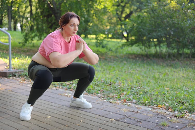 A woman in exercise gear does squats outside.