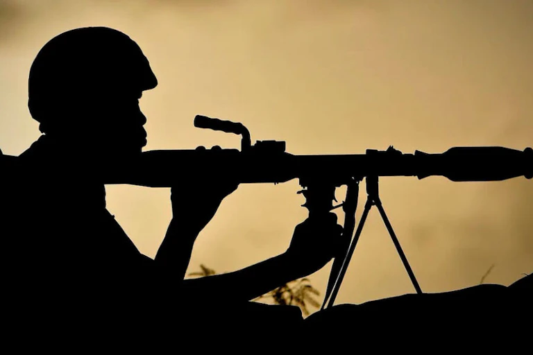 A silhoutte image of a man next to a missile-firing gun that's on the ground