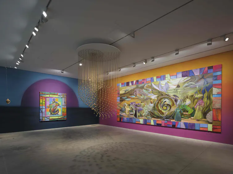 A view of two paintings and a hanging installation of bells.