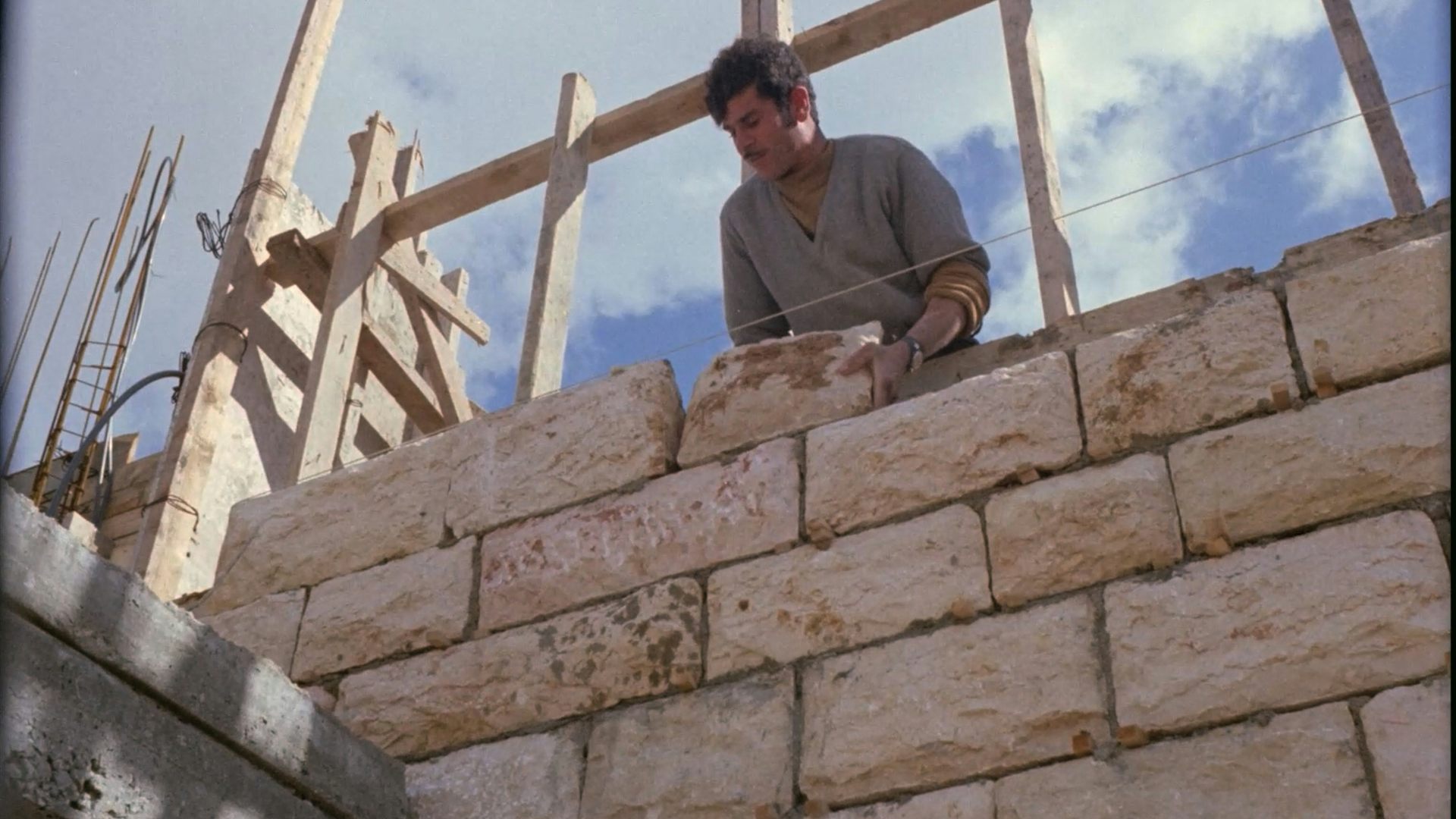 A man standing at a wall cementing large stone bricks together.