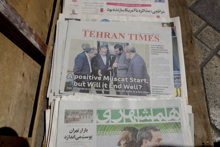 A stack of newspapers is seen with the top one showing a photo of a group of men.