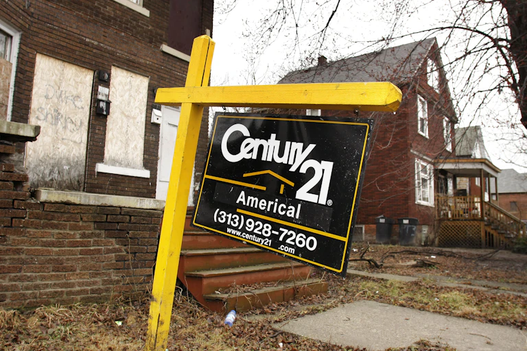 A yellow and black Century 21 realtor sign is hanging in front of a boarded-up home.