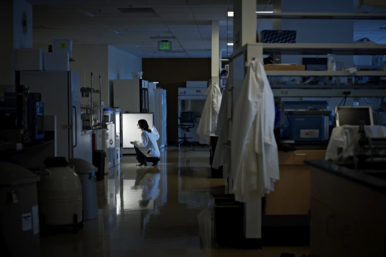 Scientist kneeling in front of a fridge in a dark research lab