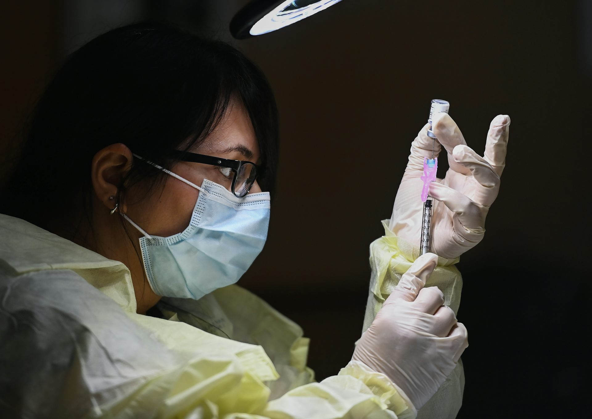 Close-up of a woman in profile in PPE gown, gloves and face mask filling a syringe