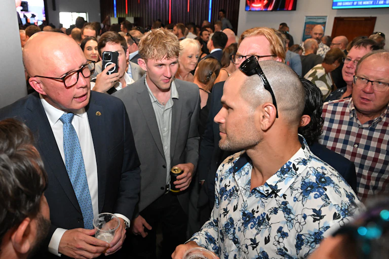 Peter Dutton dressed in a suit and blue tie, holding a beer, while talking to a crowd inside the Townsville Returned and Services League Club.