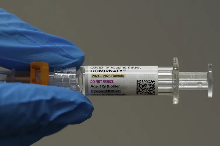 A gloved hand holding a shot of COVID-19 vaccine.