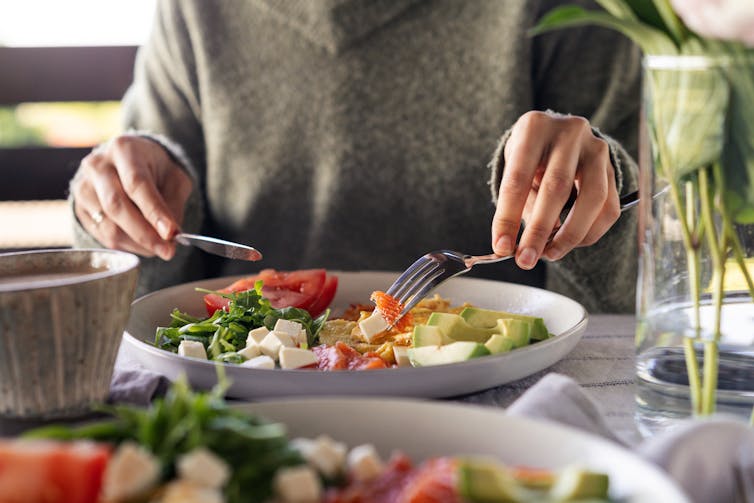 A person uses a knife and fork to eating their salad.